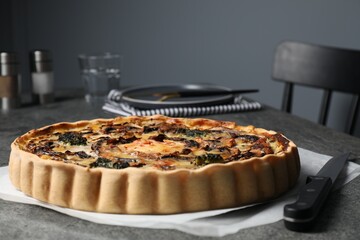 Delicious quiche with mushrooms and knife on dark grey table, closeup