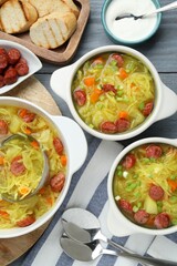 Delicious sauerkraut soup with smoked sausages and green onion served on grey wooden table, flat lay