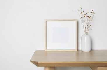 Empty photo frame and vase with dry decorative flowers on wooden table. Mockup for design