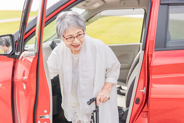 杖をついて車の助手席から降りる笑顔のシニア・高齢者女性
