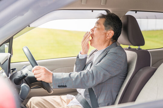 自動車の運転中に眠気を感じてあくびをする高齢者・シニア男性
