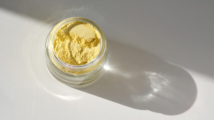 An open jar of a yellow turmeric facial scrub showing off its texture.