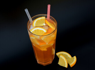 A tall glass of refreshing lemonade with ice and citrus pieces on a black background.