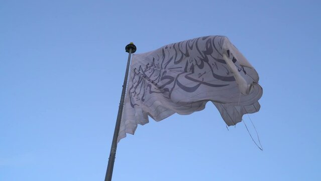 Taliban Afghanistan flag moving in wind by blue sky, ground view slomo