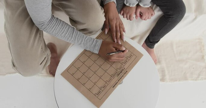 African american mother making a 30 day challenge calendar for her daughter, seen from above