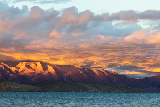 Gazing at the high-altitude lake Manasarovar at sunset in Tibet is a stunning experience. The sun's rays pierce through the clouds, casting a warm glow on the serene and smooth surface of the lake.