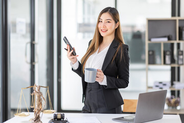 Lawyer business Asian woman office. Statue of Justice with scales and lawyer working on a laptop and using phone at workplace . Legal law, advice and justice concept.