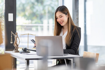 Fototapeta premium Lawyer business Asian woman office. Statue of Justice with scales and lawyer working on a laptop and using phone at workplace . Legal law, advice and justice concept.