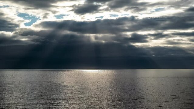 Moody time-lapse of epic sun rays over water as storm approaches darkening the sky