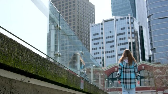 teenager girl walks along embankment against backdrop of skyscrapers of huge glass buildings back girl goes far stops and looks at nature Vancouver Canada Place Harbor Center