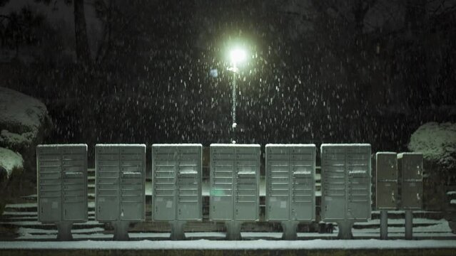 Snowy mailboxes under street light at night, winter street snowfall
