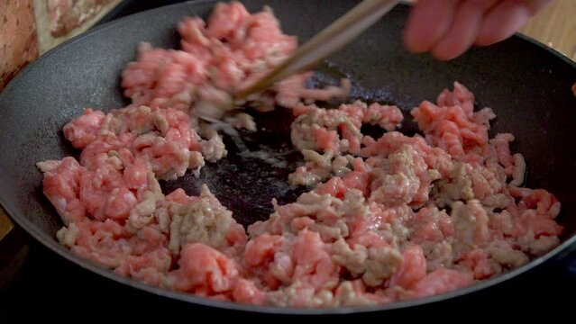Spaghetti, close-up of frying ground meat on a pan, which is being stirred with a wooden spoo