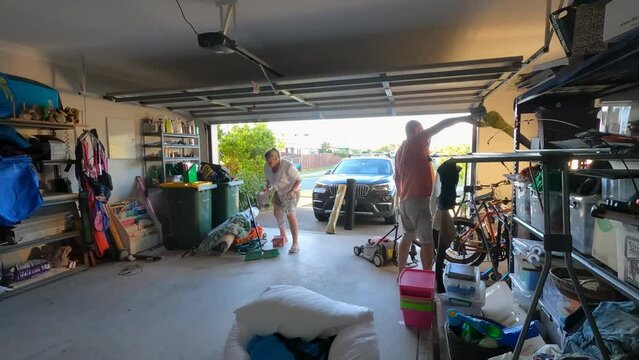 Wide shot of a Caucasian man and woman spring cleaning a double garage.