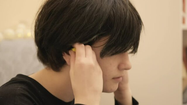 A frustrated child escapes the noisy chaos of his household by putting on bright yellow ear plugs and enjoying the silence. Closeup shot, side view.