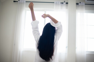 Back view of black haired woman sitting who is raising both hands of a modern luxury hotel room in the morning enjoy the sun light.