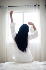 Fototapeta na wymiar Vertical picture of back view of black haired woman sitting who is raising both hands of a modern room in the morning enjoy the sun light.