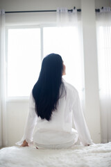 Vertical picture of the back view of a wealthy woman sitting looking out the full long window of a modern luxury apartment room in the morning enjoy the sun light.
