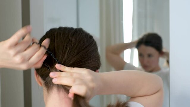 Young woman making ponytail with hair tie in front of mirror, back view.