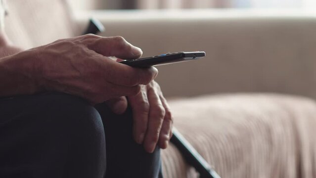 unrecognizable old man sitting on the couch and switches the buttons on the tv remote control. selective focus. the pensioner is watching television news.