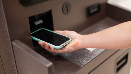 Woman using smartphone online financial transactions at ATM. NFC online banking concept. 
