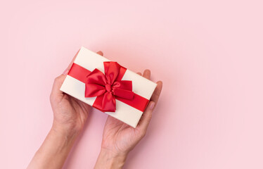 Hands holding gift box with red bow on pink background. Top view