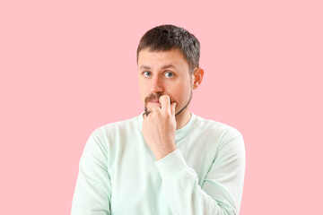 Handsome man biting nails on pink background, closeup