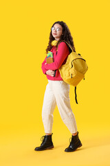 Obraz premium Female student with headphones, notebooks and backpack on yellow background