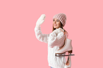 Pretty young woman with ice skates waving hand on pink background