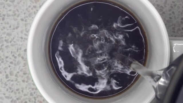 Pouring boiling water into cup of instant coffee, top down close up