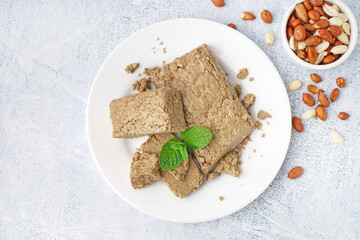 Plate with pieces of tasty halva and peanuts on light background