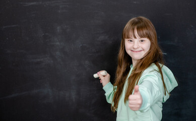Smiling young girl with Downs syndrom wants to write something on the chalkboard. Empty space for...
