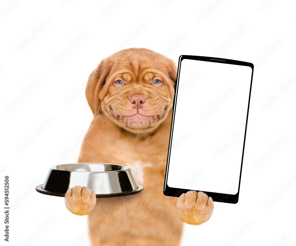 Poster Smiling puppy holding empty bowl and shows empty screen of smartphone. isolated on white background