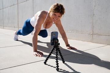 Woman filming video of herself on mobile phone while doing fitness exercises