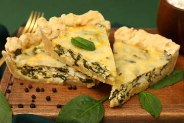 Board with pieces of delicious quiche on green background