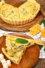 Plate and board with pieces of delicious quiche on brown wooden background