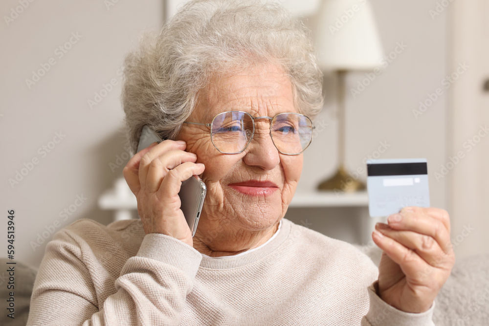 Sticker Senior woman with credit card talking by mobile phone on sofa at home, closeup