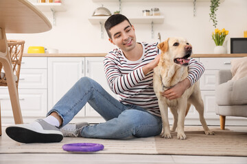 Young man with cute Labrador dog in kitchen