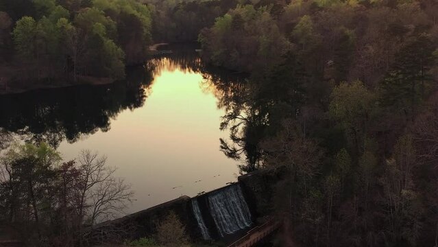 Lake Placid or water reservoir with a dam next to a forest at sunset. Paris Mountain State park. Greenville, SC. Aerial shot. 