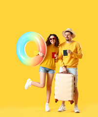 Young couple with passports, inflatable ring and suitcase on yellow background