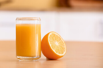 Glass of healthy juice and orange on table in kitchen