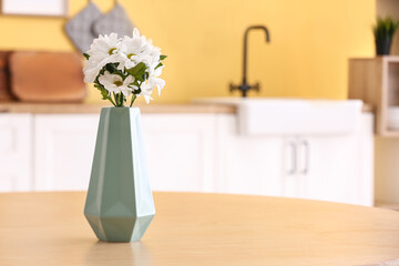 Vase with beautiful daisy flowers on table in kitchen