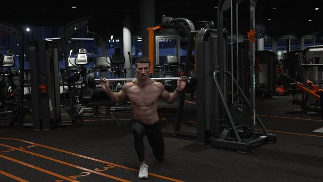 Athlete doing barbell reverse lunge in gym. Fit man exercising with barbell in fitness gym