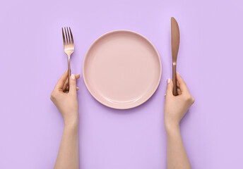 Woman with cutlery and empty plate on lilac background