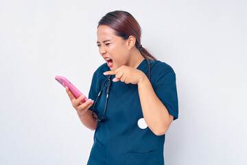 Furious young Asian woman professional nurse working wearing a blue uniform using smartphone while loudly shouting isolated on white background. Healthcare medicine concept