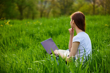 woman working on a laptop while sitting in tall grass in nature