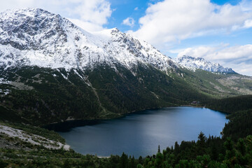 Naklejka na ściany i meble Morskie Oko Snowy Mountain Hut in Polish Tatry mountains, drone view, Zakopane, Poland. Aerial view shot of beautiful green hills and mountains in dark clouds and reflection on the lake Morskie Oko