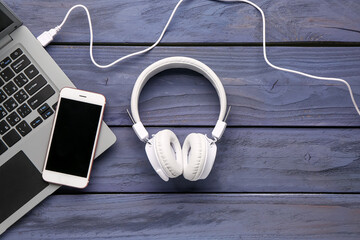 Headphones with mobile phone and laptop on dark wooden background