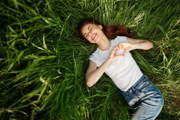 happy woman folded her arms on her chest in the shape of a heart lying in the grass