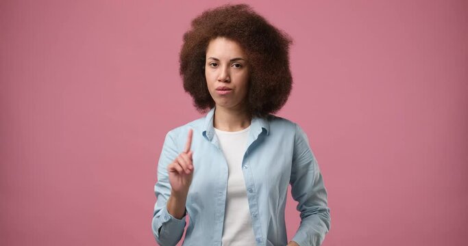 Young african american woman saying no with finger standing over pink studio background