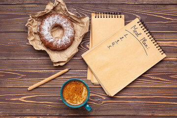 Notebooks with text MEAL PLAN, cup of coffee and cake on wooden background